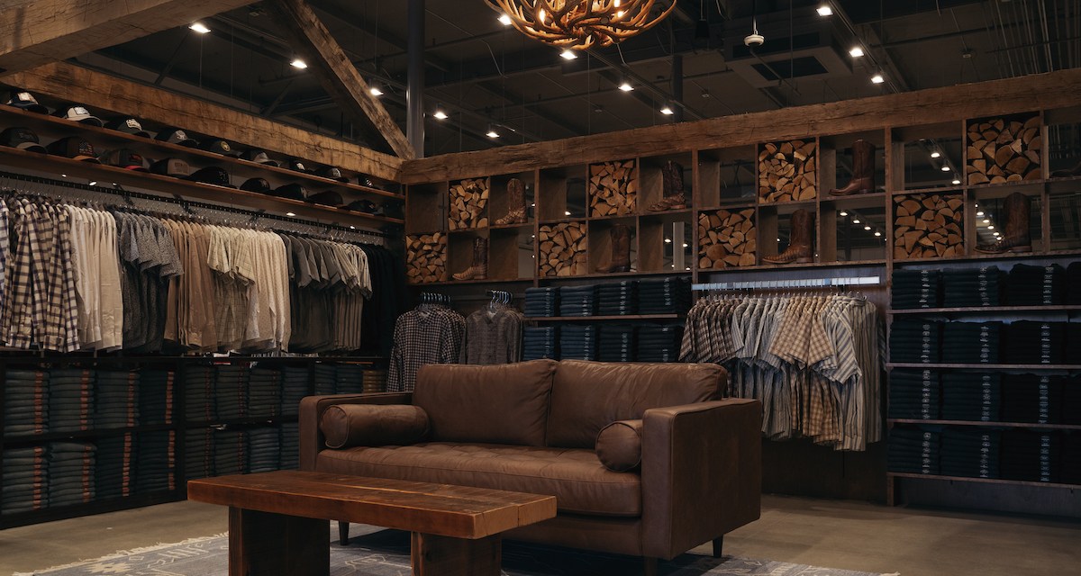 Brown leather couch and wooden side table in a retail space, surrounded by rows of button-down shirts
